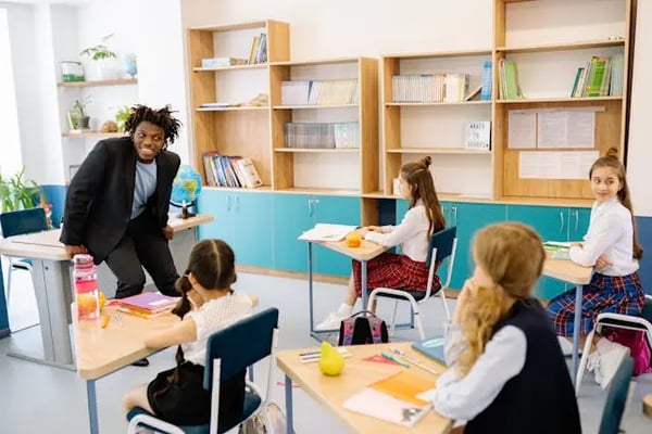 A teacher sits on his desk and talks with his class.