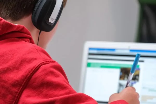 Student in red hoodie working asynchronously on laptop.