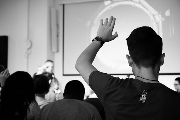 Higher ed student raising hand in class.