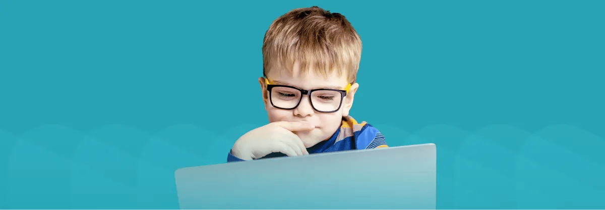 Young boy working on laptop. Teal background. 