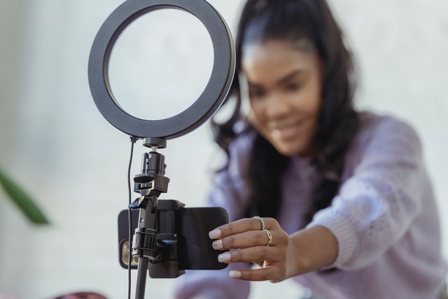 Woman adjusting cell phone sitting within standing ring light, background is blurred and ring light in focus