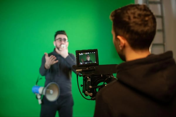 Producer shooting a man speaking into a microphone in front of a green screen.