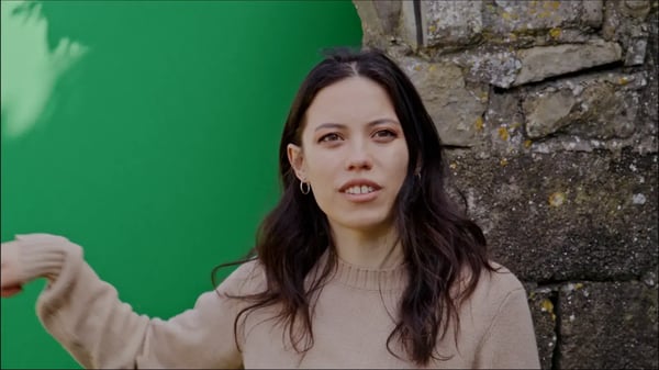 Lighting adjustment for brunette woman in brown sweater against half green screen and brown brick.