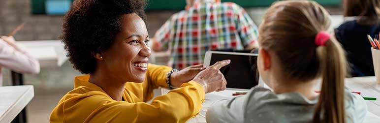 Teacher kneeling down next to student with video on tablet