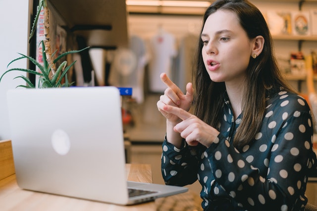 Woman gesturing with both hands while speaking in front of a laptop