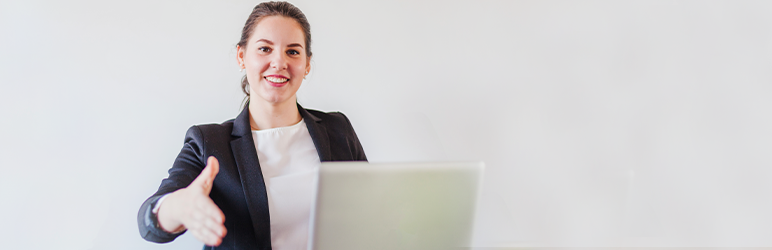 Business woman sitting in front of laptop, holding hand out for handshake. 