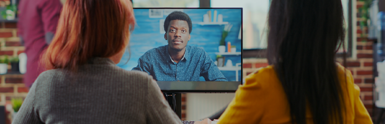 Two women sitting in front of computer watching video resume submission of young man