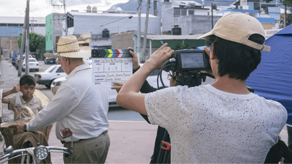 Videographer with clapperboard in front of the camera showcasing a scene with an older man approaching a child.