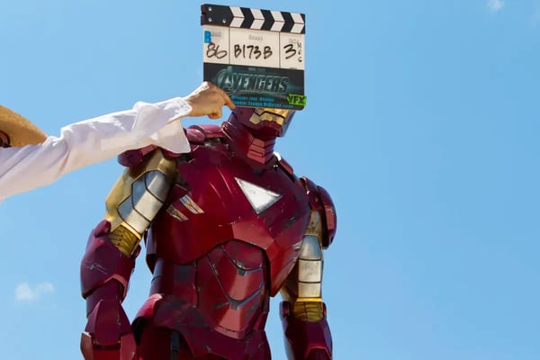 Clapperboard held in front of an Ironman character against a blue background.