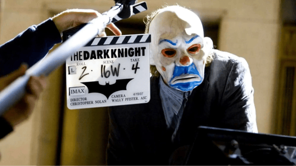 Man with joker mask on and clapperboard held in front with text, "The Dark Knight."