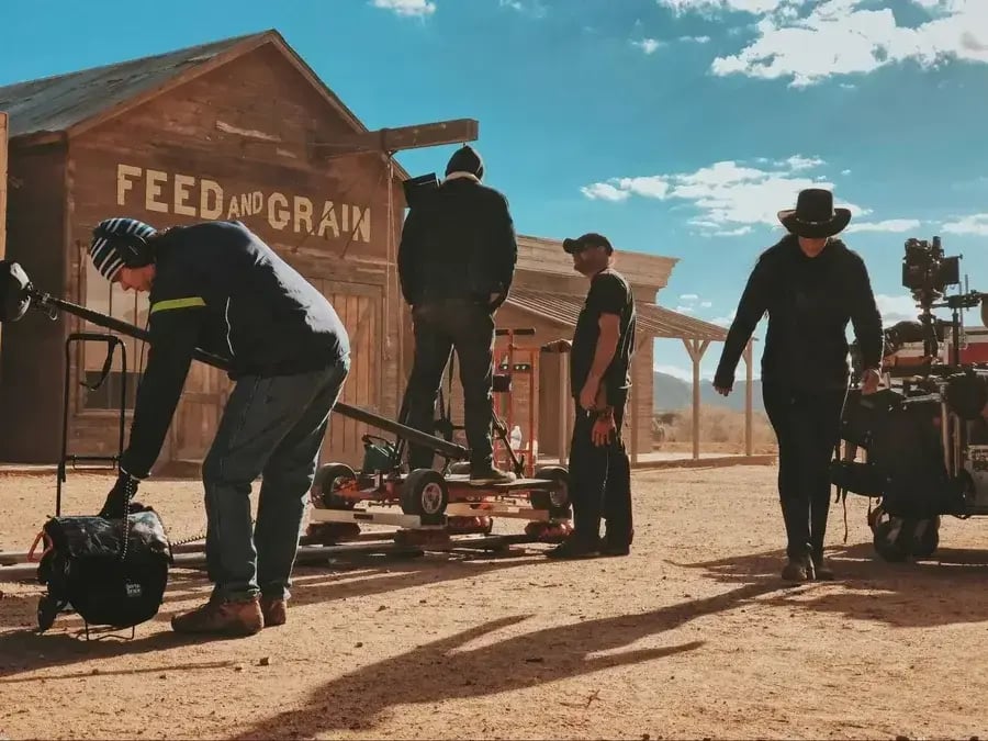 Image shows a western film set with film crew adjusting the dolly and camera.