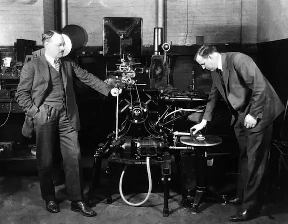 Two men working a Vitaphone to sync audio and image in black and white.