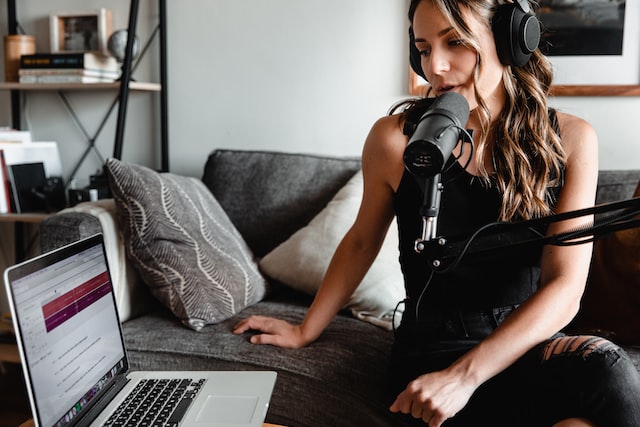 Woman sitting on sofa speaking into podcast mic looking at laptop