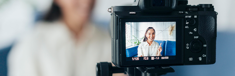 Close-up of camera on tripod, recording woman sitting on couch and giving presentation.