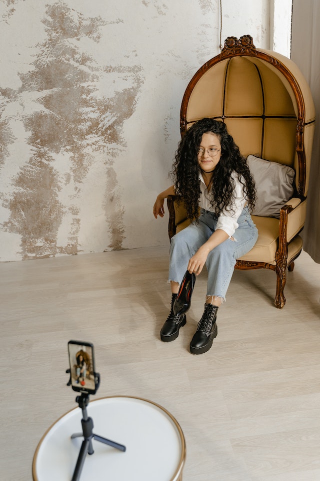 Young woman posing on vintage armchair in front of smartphone tripod