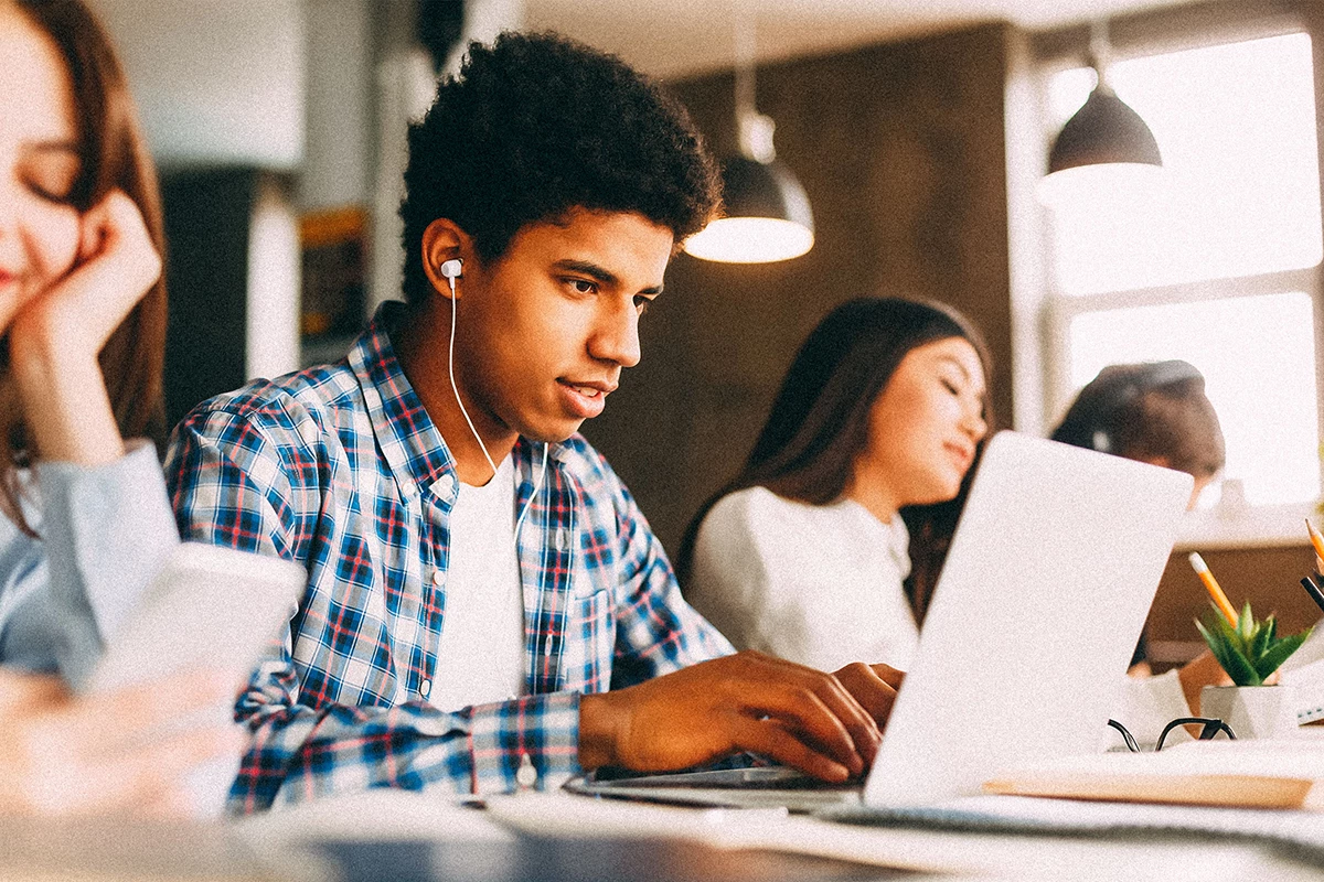 College student with headphones in ears, working on laptop.